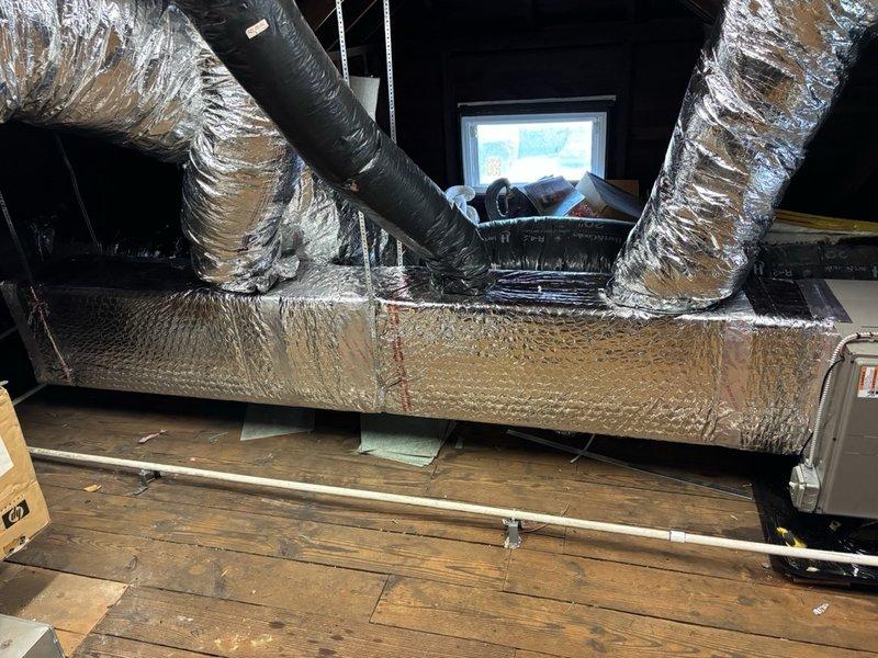 Completed installation of HVAC unit in second-floor attic space on right side of structure. Unit was positioned on proper support platform with all manufacturer specifications verified and labeled components clearly visible. Flexible aluminum ductwork was routed throughout the attic space to connect the new system, with insulated ducts extending from the unit to distribute conditioned air. Electrical control panel was mounted and wired to wall, featuring all necessary switches and control mechanisms for system operation. All ductwork was properly insulated with foil-faced reflective material to maximize energy efficiency and prevent condensation. System connections were secured, and installation was completed in accordance with manufacturer guidelines and industry standards.