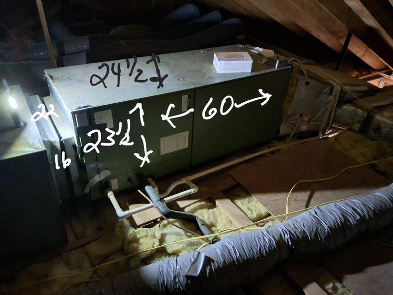 Completed AC system estimate in attic space. Documented existing green air handler unit positioned on wooden platform with exposed ductwork and insulation. Photographed equipment dimensions, duct configurations, and current installation conditions including flexible ductwork and fiberglass insulation placement for estimate preparation.