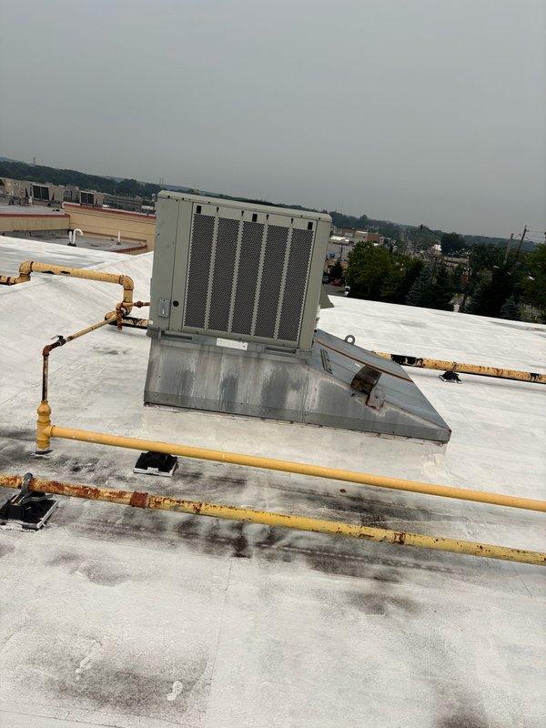 # No Cooling - Half of Store Not Maintaining Temperature

Responded to service call for commercial building experiencing uneven cooling with half of the store not maintaining proper temperature. Upon arrival, conducted rooftop inspection of multiple HVAC units serving the facility.

Inspection revealed two Trane rooftop units with significant weathering and corrosion. Primary unit showed extensive rust staining on cabinet exterior and mounting curb, with orange-brown vertical streaking concentrated on lower portions of equipment. Adjacent unit displayed similar deterioration with corroded yellow gas line routing across roof membrane showing advanced rust penetration through paint coating.

Performed operational assessment of both units to determine cause of cooling imbalance. Checked refrigerant levels, airflow, and electrical connections on affected equipment. Verified proper operation of evaporative cooling components and examined condition of mounting platforms and roof curbs for st