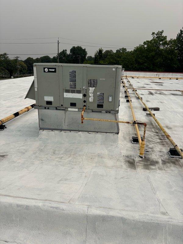 # No Cooling - Half of Store Not Maintaining Temperature

Responded to service call for commercial building experiencing uneven cooling with half of the store not maintaining proper temperature. Upon arrival, conducted rooftop inspection of multiple HVAC units serving the facility.

Inspection revealed two Trane rooftop units with significant weathering and corrosion. Primary unit showed extensive rust staining on cabinet exterior and mounting curb, with orange-brown vertical streaking concentrated on lower portions of equipment. Adjacent unit displayed similar deterioration with corroded yellow gas line routing across roof membrane showing advanced rust penetration through paint coating.

Performed operational assessment of both units to determine cause of cooling imbalance. Checked refrigerant levels, airflow, and electrical connections on affected equipment. Verified proper operation of evaporative cooling components and examined condition of mounting platforms and roof curbs for st