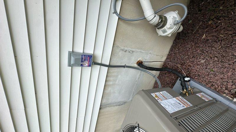 Completed full replacement of residential 3.5 ton air conditioning system with new 14.3 SEER2 unit utilizing R-454B refrigerant. Removed existing outdoor condenser unit and installed new equipment on existing concrete pad adjacent to building exterior. Mounted electrical disconnect box on siding with proper conduit routing to new condenser. Installed and secured refrigerant line set along exterior wall using appropriate mounting brackets and weatherproofing measures. Connected PVC condensate drainage system with flexible tubing to ensure proper discharge. Interior installation included connection to existing duct plenum system and integration with HVAC equipment in mechanical space. Ran all necessary electrical wiring and control cables to ensure proper system operation. Verified all refrigerant connections are secure and leak-free. System tested and confirmed operational with proper airflow and cooling capacity.