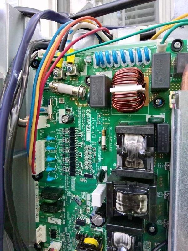 Continued diagnostic and repair work on mini-split system, focusing on the main control board assembly. Inspected and photographed the PCB within the electrical enclosure, documenting various electronic components including the toroidal inductor, capacitors, transformers, relays, and wire connections to terminal blocks. Verified proper mounting of circuit board within metal chassis and examined all wire harnesses and connector housings for secure connections and proper routing.