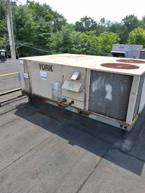 Conducted comprehensive assessment of two existing rooftop HVAC units for replacement estimate. Both York RTUs showed significant age-related deterioration including extensive rust staining, weathered exterior panels, and corroded base components. Documented current equipment conditions through detailed photography, noting unit specifications, electrical disconnects, and mounting configurations. Evaluated rooftop membrane condition, curb adapters, and accessibility requirements for future replacement work.