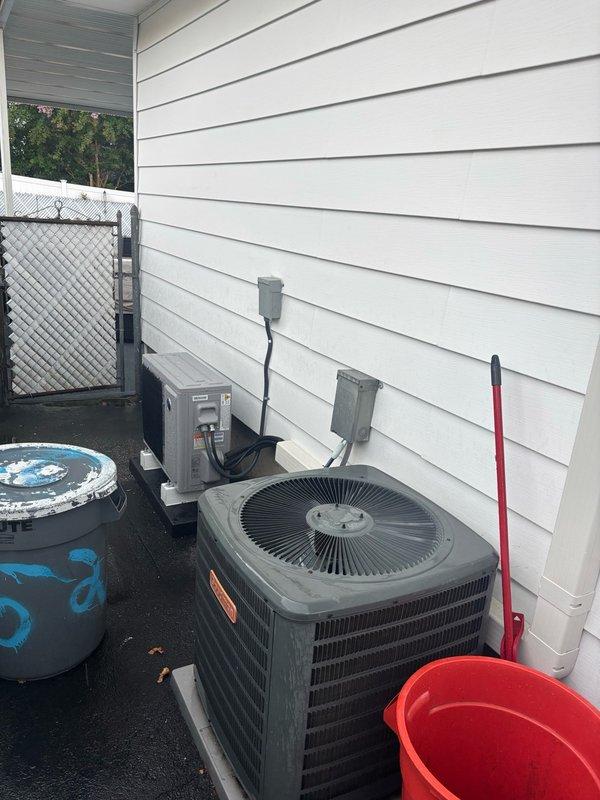 Completed walkthrough and documentation of newly installed split-system HVAC equipment at residential property. Photographed exterior condenser unit positioned against building with proper clearance, including two electrical disconnect boxes mounted on siding with appropriate conduit routing. Documented interior wall-mounted air handler unit installed in garage space with organized refrigerant line set and electrical conduit properly secured to wall-mounted shelving system. Captured nameplate information from new equipment as requested for warranty and service records.