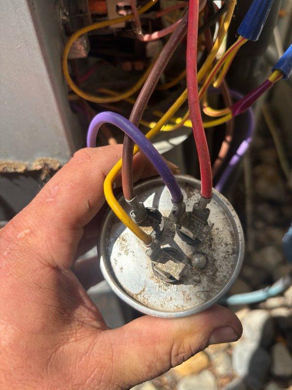 Replaced failed condenser unit and installed new capacitor to restore system functionality. Removed old weathered capacitor showing significant corrosion, oxidation at terminal points, and accumulated environmental debris that compromised electrical connections. Connected new capacitor with proper wire configuration including brown, red, yellow, purple, and blue leads, ensuring secure terminal connections and verifying all electrical specifications matched system requirements for safe operation.