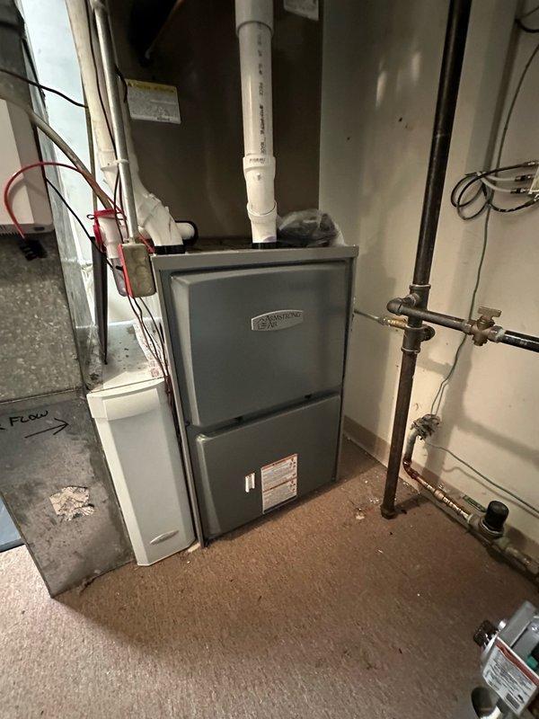 Completed residential furnace replacement in basement utility room. Removed existing heating unit and installed new gray metal furnace system with proper venting, including white PVC exhaust pipe routed vertically through ceiling. Connected gas supply lines with appropriate shut-off valves and verified all copper piping connections for secure operation. System tested and confirmed operational upon completion.