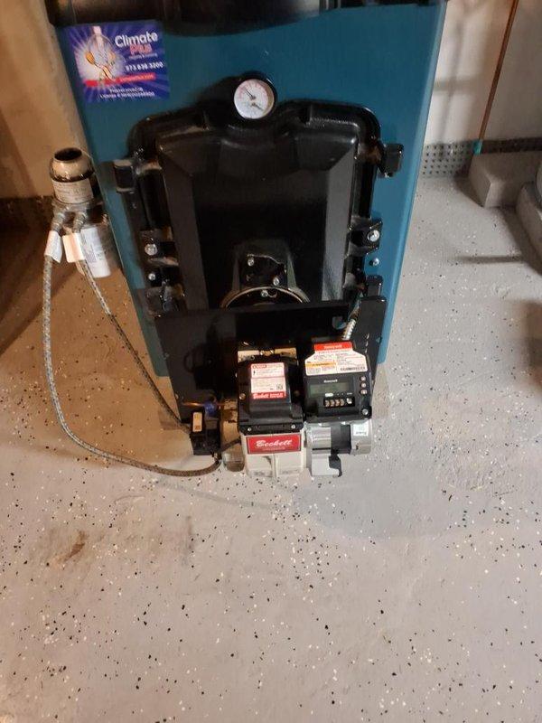 Completed seasonal maintenance on oil-fired hydronic heating system with teal-cased boiler unit. Performed comprehensive inspection of burner assembly, verified proper operation of all controls including digital display and pressure gauge, checked all copper piping connections and fittings for leaks, inspected expansion tank mounting and integration, and confirmed proper function of circulator pump and zone valves. All system components operating within normal parameters.