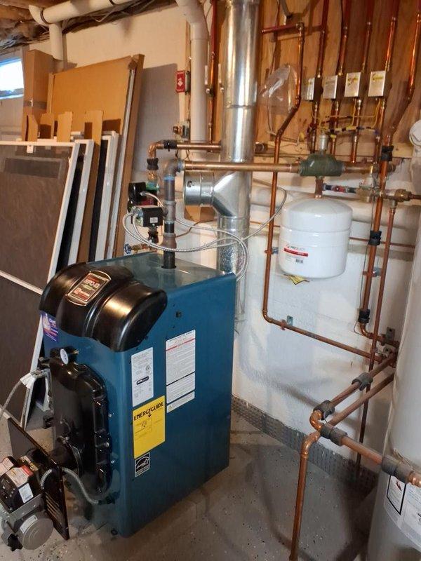 Completed seasonal maintenance on oil-fired hydronic heating system with teal-cased boiler unit. Performed comprehensive inspection of burner assembly, verified proper operation of all controls including digital display and pressure gauge, checked all copper piping connections and fittings for leaks, inspected expansion tank mounting and integration, and confirmed proper function of circulator pump and zone valves. All system components operating within normal parameters.