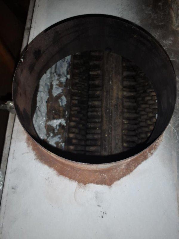 Completed maintenance inspection on oil boiler system and investigated customer complaint of exhaust odors entering the living space during operation. Upon inspection, discovered significant deterioration and staining around the barometric damper assembly, with visible rust, corrosion, and accumulated debris on the surrounding surfaces indicating potential breach in the flue system integrity. Documented conditions with photographs showing compromised sealing and excessive wear on damper components, which likely allows combustion gases to escape into the occupied space rather than being properly vented through the chimney. Advised customer of safety concerns and recommended immediate repair or replacement of the barometric damper assembly and inspection of the entire venting system to eliminate hazardous exhaust infiltration.