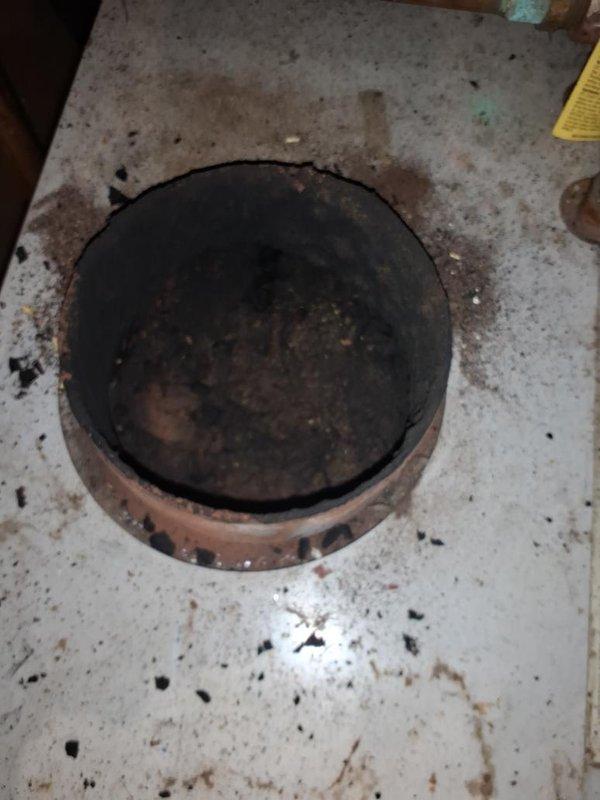 Completed maintenance inspection on oil boiler system and investigated customer complaint of exhaust odors entering the living space during operation. Upon inspection, discovered significant deterioration and staining around the barometric damper assembly, with visible rust, corrosion, and accumulated debris on the surrounding surfaces indicating potential breach in the flue system integrity. Documented conditions with photographs showing compromised sealing and excessive wear on damper components, which likely allows combustion gases to escape into the occupied space rather than being properly vented through the chimney. Advised customer of safety concerns and recommended immediate repair or replacement of the barometric damper assembly and inspection of the entire venting system to eliminate hazardous exhaust infiltration.