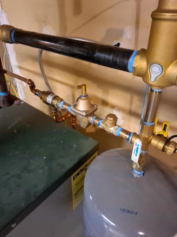 Responded to call for water leak originating from boiler system. Upon inspection, identified leak at brass pressure regulator assembly and connection joints on supply piping. Tightened compression fittings at blue-taped connection points and verified proper seating of braided flexible hose connections. Inspected Peerless boiler unit, expansion tank, and associated copper piping for additional moisture or compromised joints. Tested system under pressure, confirmed leak was resolved, and verified all valves and pressure gauge readings were within normal operating parameters.