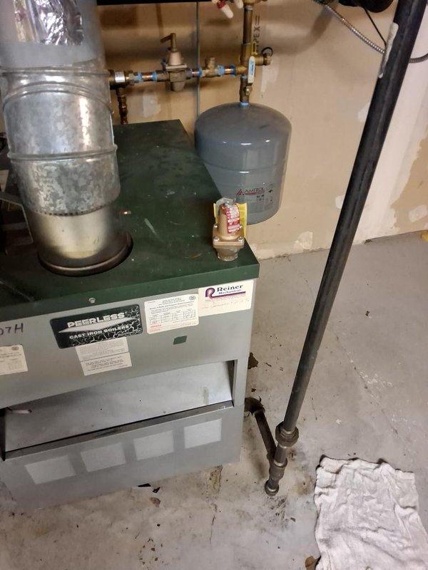 Responded to call for water leak originating from boiler system. Upon inspection, identified leak at brass pressure regulator assembly and connection joints on supply piping. Tightened compression fittings at blue-taped connection points and verified proper seating of braided flexible hose connections. Inspected Peerless boiler unit, expansion tank, and associated copper piping for additional moisture or compromised joints. Tested system under pressure, confirmed leak was resolved, and verified all valves and pressure gauge readings were within normal operating parameters.