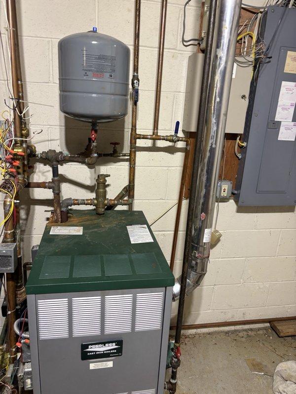 Responded to a no-heat call on a Peerless cast iron boiler, where the system was firing but failing to bring the home above 61°F despite a raised thermostat setpoint and good thermostat batteries. Inspection of the boiler and near-boiler piping revealed corrosion, discoloration, and rust staining at the copper piping and connections on top of the boiler, indicating a likely leak or water-side issue affecting heat output. The condition was documented with photos, and further repair of the affected piping and connections is recommended to restore reliable heat delivery.