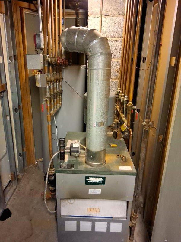 Responded to a no-heat call on an aged cast iron boiler and inspected the unit, flue, and associated piping and valves. Documented heavy corrosion and oxidation on the copper supply piping and isolation valve, along with rust and mineral deposits at the base of the piping, indicating long-term leakage and age-related deterioration. The boiler's condition and component wear were noted as the cause of the heat loss, with replacement recommended to restore reliable heating.