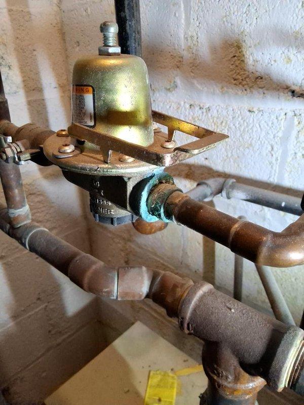 Responded to a no-heat call for a non-operating boiler and inspected the mechanical room piping, pressure-reducing valve, and associated valve assemblies. Found verdigris corrosion at the threaded joints of the pressure-reducing valve and adjacent copper piping, along with mineral deposits indicating past seepage at brass fittings and the valve body threads. Documented all findings with photos for review and recommended repair or replacement of the corroded fittings and valve connections to restore reliable system operation.