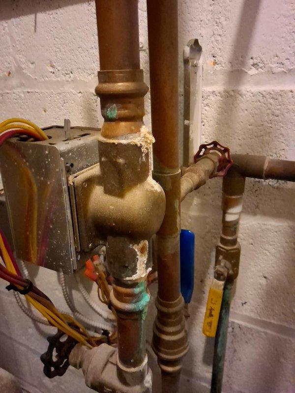 Responded to a no-heat call for a non-operating boiler and inspected the mechanical room piping, pressure-reducing valve, and associated valve assemblies. Found verdigris corrosion at the threaded joints of the pressure-reducing valve and adjacent copper piping, along with mineral deposits indicating past seepage at brass fittings and the valve body threads. Documented all findings with photos for review and recommended repair or replacement of the corroded fittings and valve connections to restore reliable system operation.