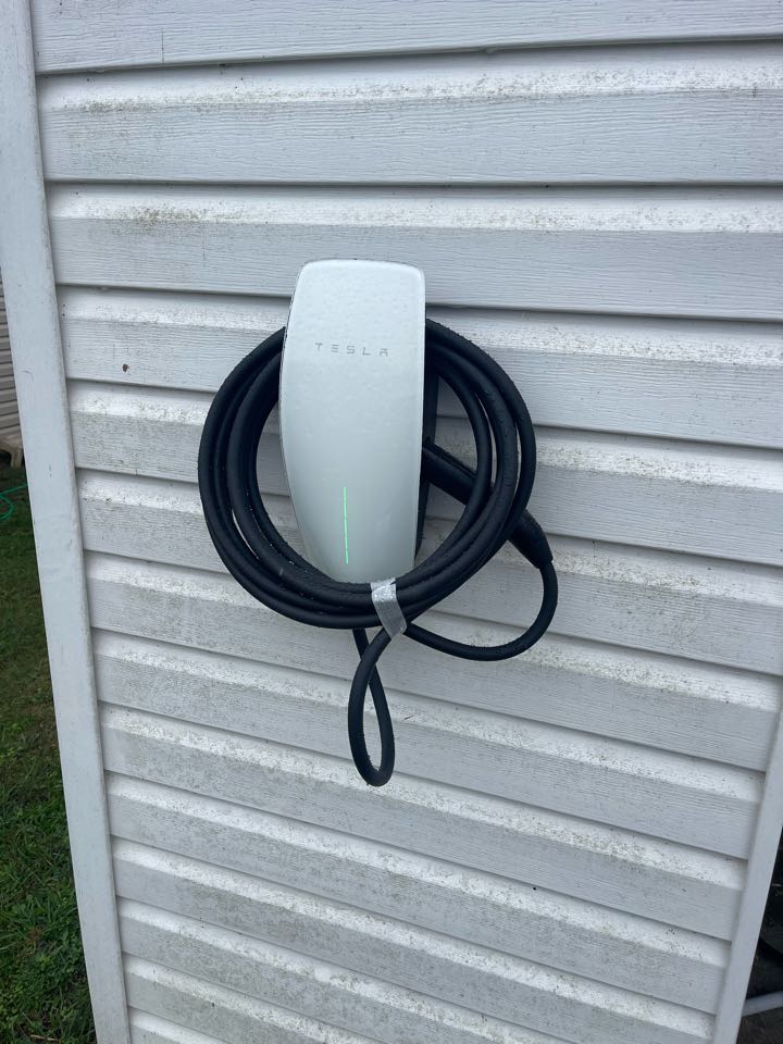 Electrician is installing a new outdoor mounted Tesla charging port 