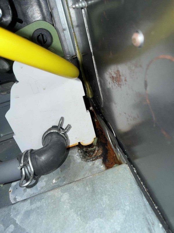Diagnosed water leak under 8-year-old basement furnace connected to humidifier system. Inspection revealed significant corrosion and rust formation at drain connection point, with deterioration visible at the humidifier reservoir connection to metal surface. Replaced damaged drain hose and connection components to resolve the leak while maintaining proper system operation.