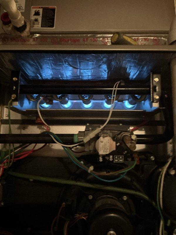 Responded to service call for furnace with yellow LED indicator light. Performed diagnostic inspection revealing normal operation of burner assembly with proper blue flame pattern across all six ports. Verified electrical connections and plumbing components were intact and functioning correctly; system now operating within normal parameters.