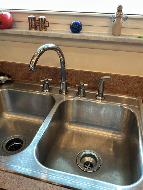 Returned to residence to complete previously scheduled kitchen faucet installation. Successfully installed new chrome dual-handle faucet with side sprayer in double-basin stainless steel sink. Verified proper water flow and absence of leaks after installation, leaving work area clean.