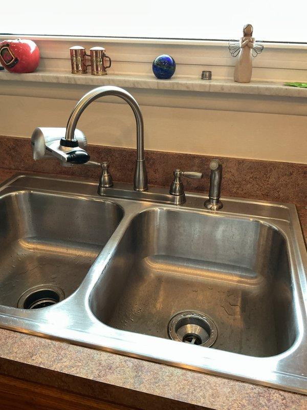 Returned to residence to complete previously scheduled kitchen faucet installation. Successfully installed new chrome dual-handle faucet with side sprayer in double-basin stainless steel sink. Verified proper water flow and absence of leaks after installation, leaving work area clean.
