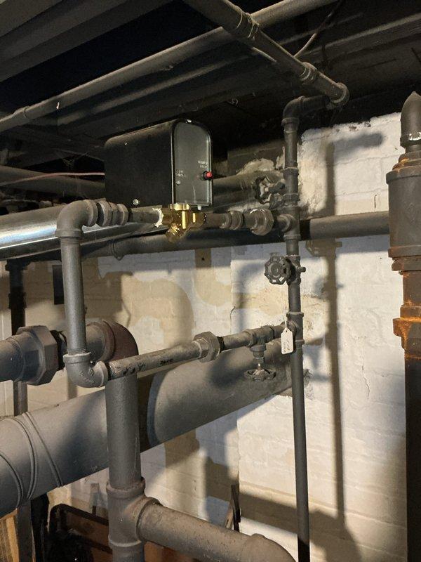 Conducted comprehensive inspection on 30-year-old steam boiler system (1989 model) located in basement. Identified unit as completely sooted up requiring service. Inspection included evaluation of associated components including Nest thermostat, humidifier, and hot water tank. Documentation of plumbing infrastructure and control systems completed with photographic evidence.