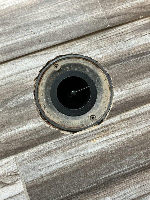 Conducted visual inspection of pressure gauge and floor drain components on wood-grain surface. Both fixtures showed signs of normal wear with minor deterioration around the edges. No immediate action required as all components appear to be functioning properly despite cosmetic aging.