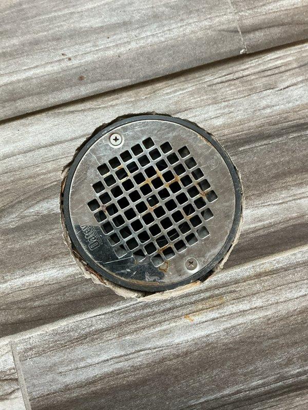 Conducted visual inspection of pressure gauge and floor drain components on wood-grain surface. Both fixtures showed signs of normal wear with minor deterioration around the edges. No immediate action required as all components appear to be functioning properly despite cosmetic aging.