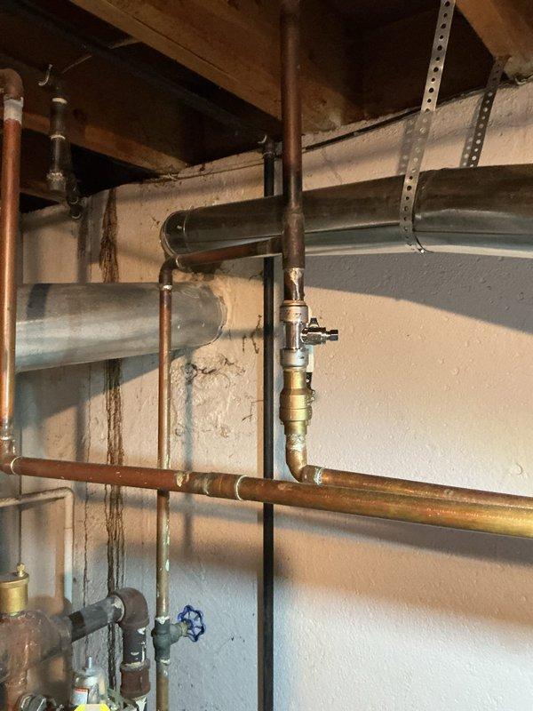 Performed comprehensive inspection of 16+ year old hot water boiler system located in basement. Examined copper supply lines, brass valves, and ventilation connections, finding all components in functional condition despite age-related discoloration. Inspected Bradford White water heater with attached copper piping and flue connections, confirming proper installation and operation with no visible leaks or damage present.