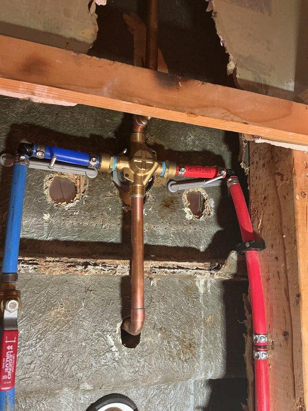 Completed installation of a dual-head shower system in bathroom with main fixed showerhead and secondary handheld unit, both in brushed nickel finish. Accessed and worked on plumbing connections within wall cavity, properly connecting the brass mixing valve to hot (red) and cold (blue) water supply lines. Documented installation with photos showing both the completed fixture and the properly connected plumbing components behind the wall.