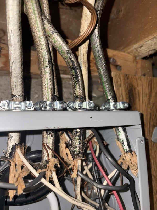 Addressed City of Warren electrical violations by installing proper ground rods below grade, cleaning and securing water ground connections to pipe, installing correctly sized overcurrent protection for #12-#14 circuits, and ensuring all NMB cable jackets terminate at least 1/4" inside the panel. Documentation photos show deteriorated wiring insulation requiring replacement and proper water ground connection installation at the copper plumbing system.