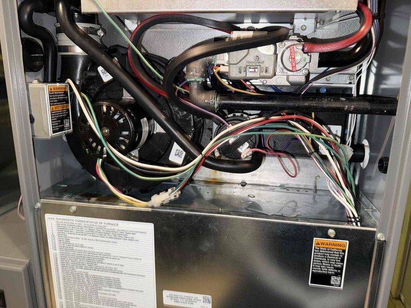 Diagnosed high pressure switch issue on thermostat of one-year-old HVAC system located in lower level. System remains operational for both heating and cooling functions despite the fault. Documented system condition with photos of plumbing components and interior furnace assembly including wiring connections. Parts ordered through Lennox under PO: 1287586-001.