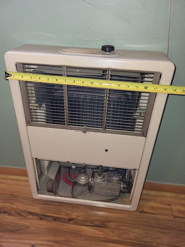 Performed inspection and evaluation of a non-functional 67-year-old wall-mounted gas space heater in the back bedroom. Unit is approximately 15-16 inches wide by 13-14 inches high, mounted on a mint green wall above wooden flooring. Measurements were taken and documentation photos captured to prepare replacement estimate for a new gas-powered wall heater with exterior venting capabilities.