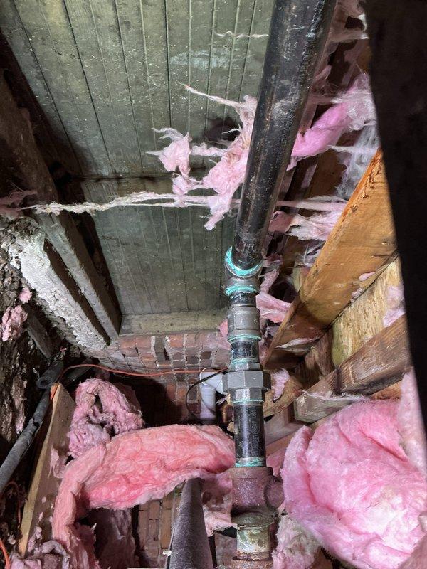 Completed steam line repairs in confined structural space, addressing deteriorated sections where insulation was compromised. Installed new vertical cast iron pipe with proper connections against brick wall, securing all components with appropriate fasteners and ensuring system integrity for continued operation.