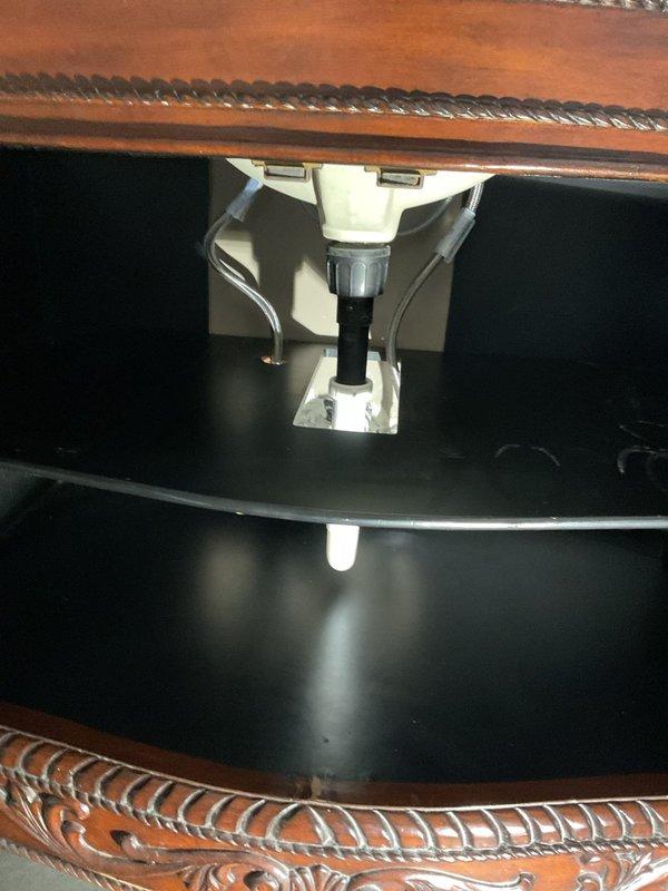 Completed installation of a new faucet in customer's bathroom, requiring removal of the existing fixture and proper connection to the under-sink plumbing system. Successfully installed and secured the dark basin/sink to the wooden counter using appropriate mounting hardware, and connected the white PVC drain assembly with P-trap configuration. All connections were tested for leaks and proper drainage.