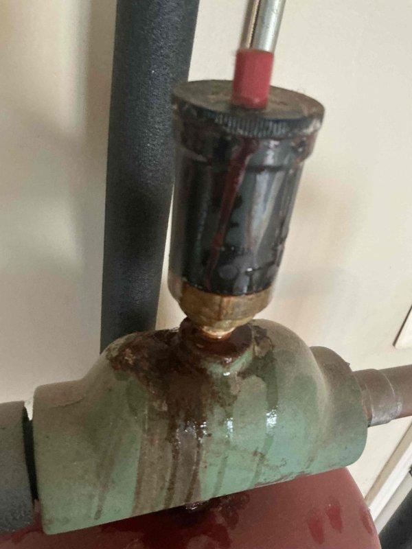 Responded to customer complaint of boiler cycling without producing heat. Inspection revealed significant corrosion and deterioration of valve components, particularly a green valve body with extensive rust and streaking indicative of moisture damage. Noted substantial corrosion along plumbing pipes in utility room with compromised connections that prevented proper system operation.