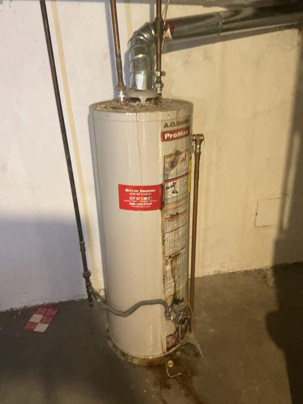 Replaced 40-gallon A.O. Smith ProMax water heater in basement that showed significant rust damage and leakage evidenced by water stains on concrete floor. Installation included proper venting connections, supply line hookups, and installation of required drip pan to prevent future water damage.