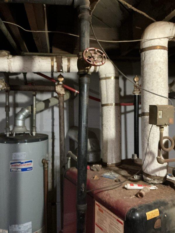 Conducted a comprehensive boiler estimate in residential utility room, documenting an American brand water heater system with associated plumbing components. Inspection revealed an older furnace/boiler unit with connecting copper pipes, valves and fittings, with particular attention paid to a valve connection on PVC piping that was highlighted for potential service.