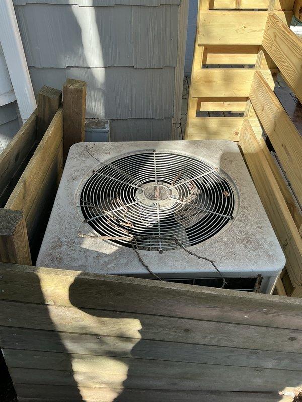 Performed inspection of residential property to generate replacement estimate for 50+ year old HVAC system. Observed outdated furnace and AC unit located in basement, with exterior condenser showing significant deterioration including cracked concrete top and weathered components. Documented existing wooden enclosure surrounding outdoor unit which will need modification during replacement to accommodate modern equipment specifications.