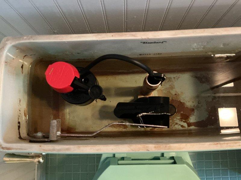 Diagnosed intermittent running toilet in upper bathroom of tri-level home. Inspected internal tank components, which revealed significant mineral buildup and corrosion on the flush valve assembly and copper components. Replaced worn flush valve and flapper to resolve the leak issue, restoring proper water shutoff function.