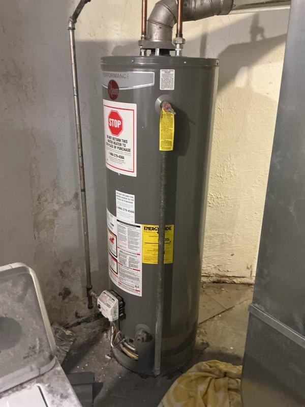 Responded to service call for a Rheem Performance water heater leaking from the bottom in basement location. Diagnostic inspection confirmed tank failure after approximately 10+ years of service, evidenced by water pooling on concrete floor. Recommended full replacement of unit due to age and irreparable tank deterioration.