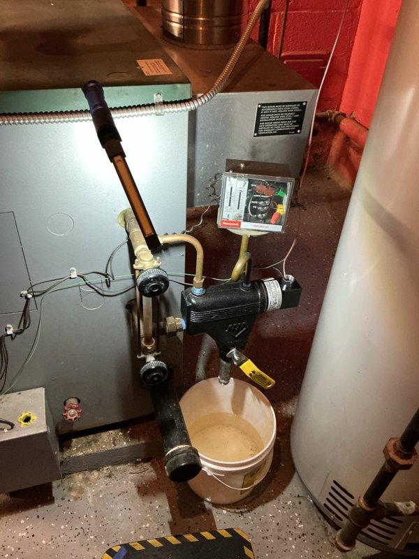 Responded to service call for boiler system maintenance. Identified water leakage from pipe junction requiring temporary collection in bucket, evidenced by brownish water drainage. Inspected VAT monitoring system (displaying "005") and associated valves/piping network, noting minor corrosion at connection points that will require follow-up service.