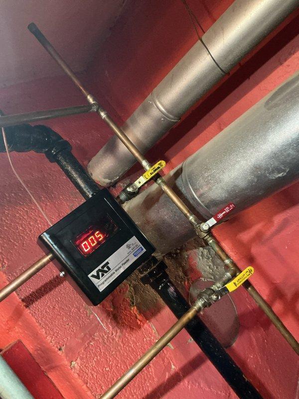 Responded to service call for boiler system maintenance. Identified water leakage from pipe junction requiring temporary collection in bucket, evidenced by brownish water drainage. Inspected VAT monitoring system (displaying "005") and associated valves/piping network, noting minor corrosion at connection points that will require follow-up service.