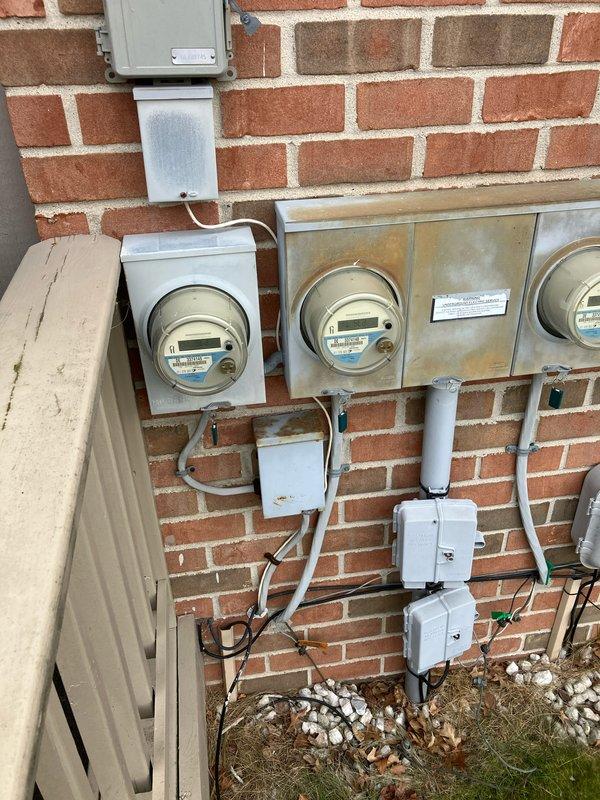 Conducted inspection of a 19-year-old furnace with failed secondary heat exchanger located in customer's basement. Documented existing outdoor AC unit positioned on gravel bed with decorative stone border adjacent to brick exterior wall. Photographed electrical service installation including four digital electric meters and associated junction boxes. Prepared comprehensive replacement options for furnace-only and complete furnace/AC system replacement as alternative to costly repairs on aging equipment.