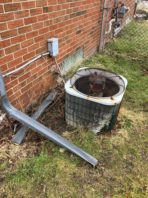 Performed assessment of 12-year-old air conditioning system that is still operational but showing significant signs of aging. Outdoor condenser unit exhibits visible rust on top cover and fan grill with weathered components. Documented existing electrical setup including junction box connections and meter configuration for replacement planning.