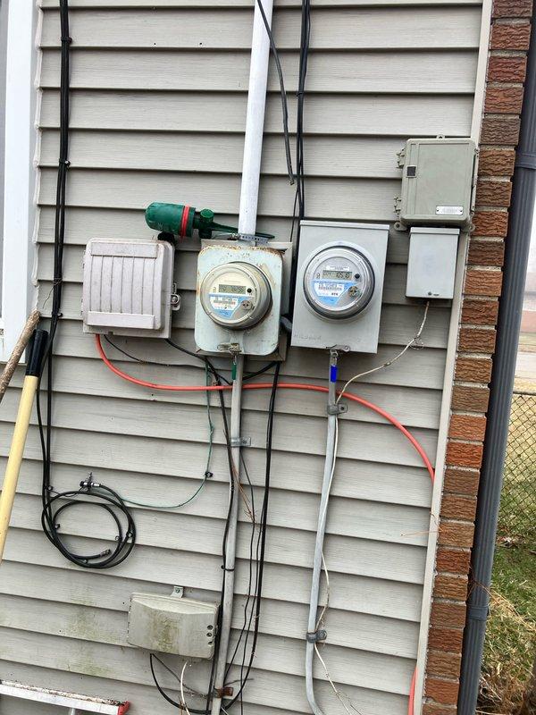 Performed assessment of 12-year-old air conditioning system that is still operational but showing significant signs of aging. Outdoor condenser unit exhibits visible rust on top cover and fan grill with weathered components. Documented existing electrical setup including junction box connections and meter configuration for replacement planning.