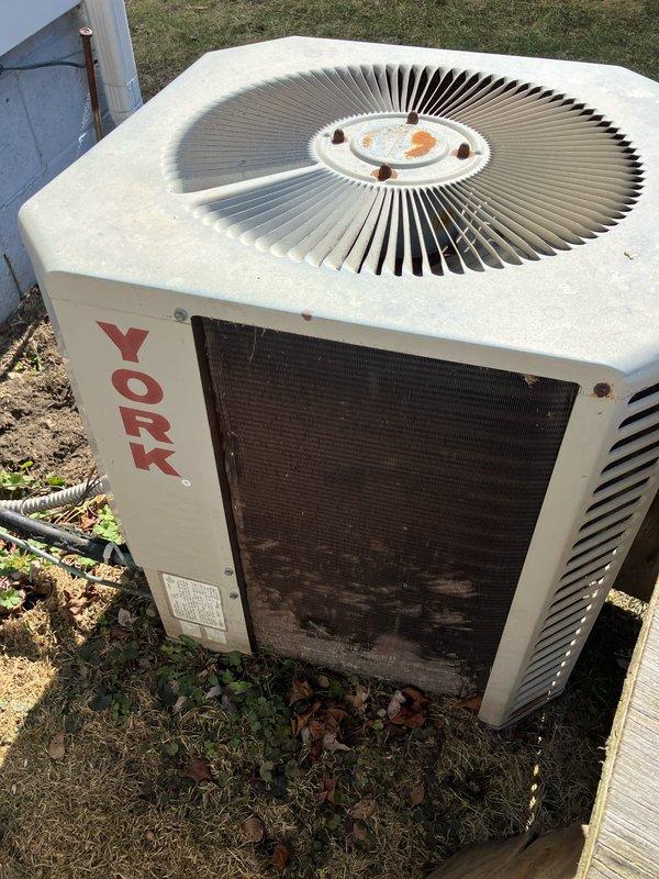 Inspected 20+ year old natural gas furnace located in crawl space under house; unit is currently operational but approaching end of service life. Exterior assessment revealed weathered York AC unit with significant rust on fan cover, dirt/residue buildup on coil cover, and deteriorated condition consistent with age. Provided replacement options for complete system upgrade to improve efficiency and reliability.