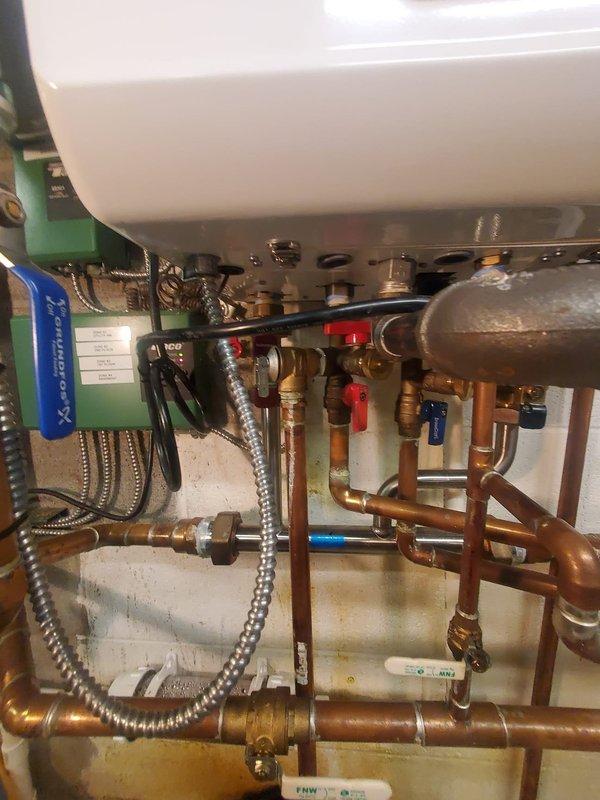 Inspected 2021 Navien combi boiler system reporting water leak. Verified leak location at copper pipe connection point near the main unit. Tightened braided stainless steel connection and checked all valves (red/blue handle shutoffs) for proper operation. System now functioning without leaks; recommended annual maintenance to prevent future issues.