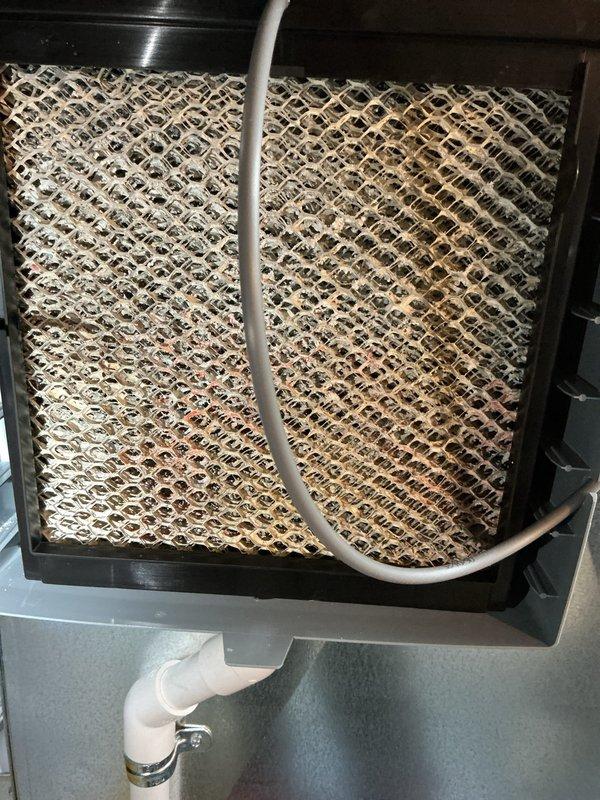 Responded to service call for a 6-month-old furnace with humidifier issues causing increased water bills. Inspected AprilAire humidifier and found evaporative pad heavily contaminated with mold and mineral buildup requiring replacement. Cleaned drainage system to address continuous water flow to laundry tub and adjusted humidistat settings to prevent excessive operation.