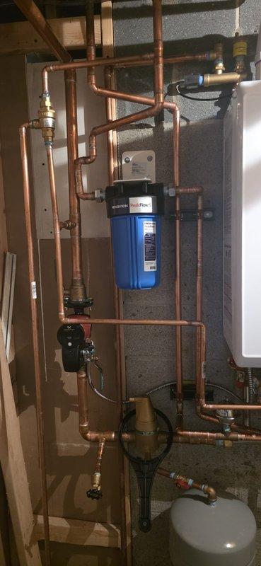 Completed installation of Navien boiler system with comprehensive copper pipe network in mechanical room. Identified factory defect in the Pentair water filtration unit for domestic hot water side showing cracking at threads and leakage. Replacement Peak Flow S filter has been ordered and will require follow-up visit for proper installation.